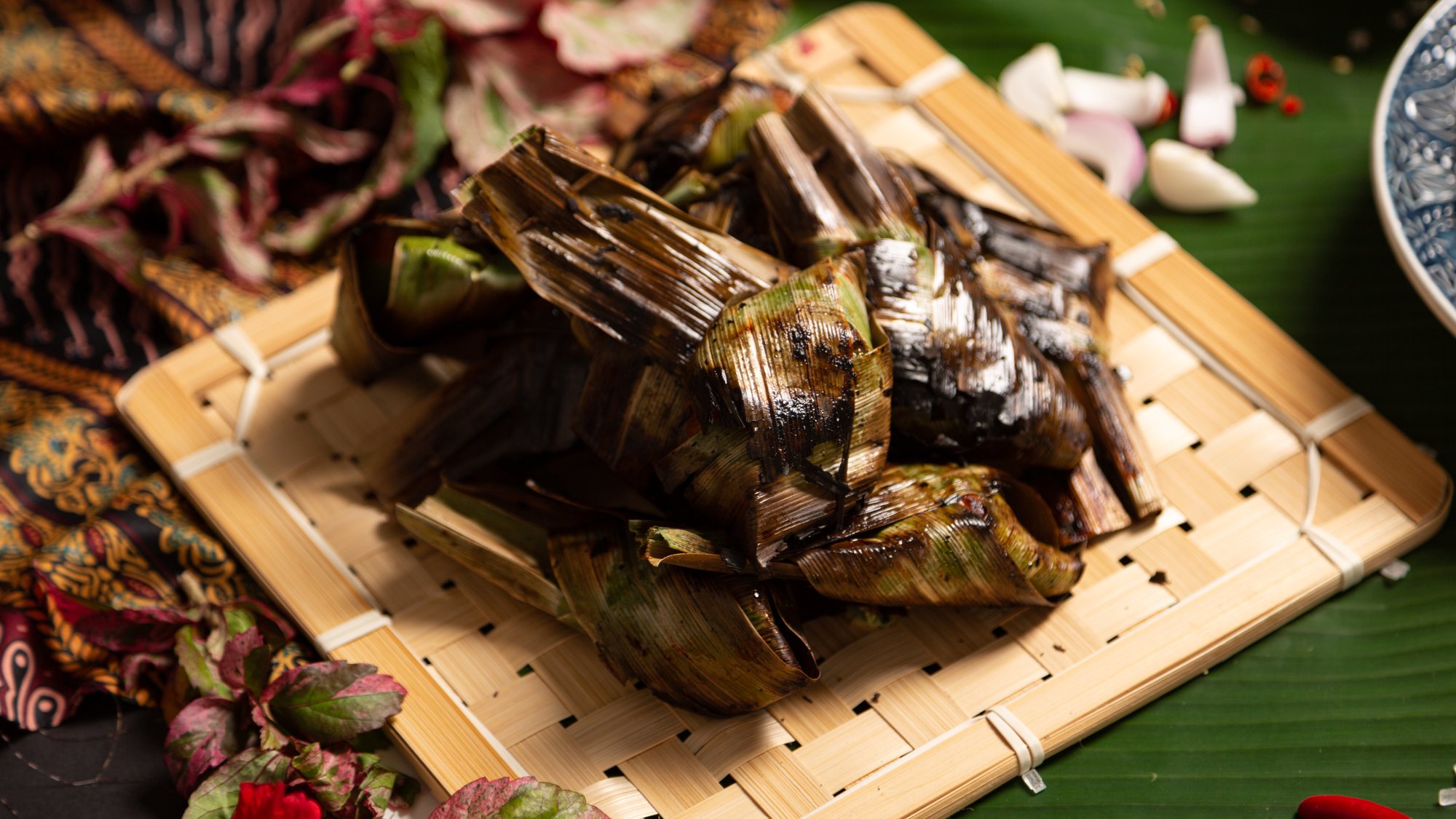 Otak-otak parcels stacked on a woven tray over banana leaf